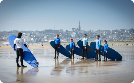 A group of people in wetsuits receiving surfing instruction on a sandy beach.