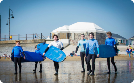 A group of people in wetsuits holding surfboards on a sunny beach.