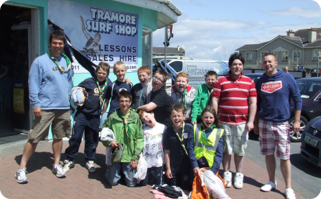 A group of children and adults posing outside the Tramore Surf Shop on a sunny day.